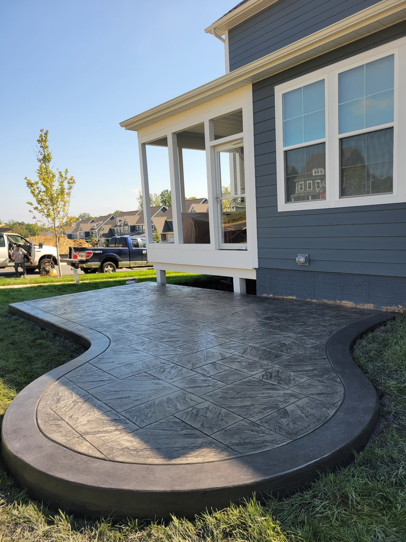 Curved stamped concrete patio alongside a screened porch on a newly built home in South Riding
