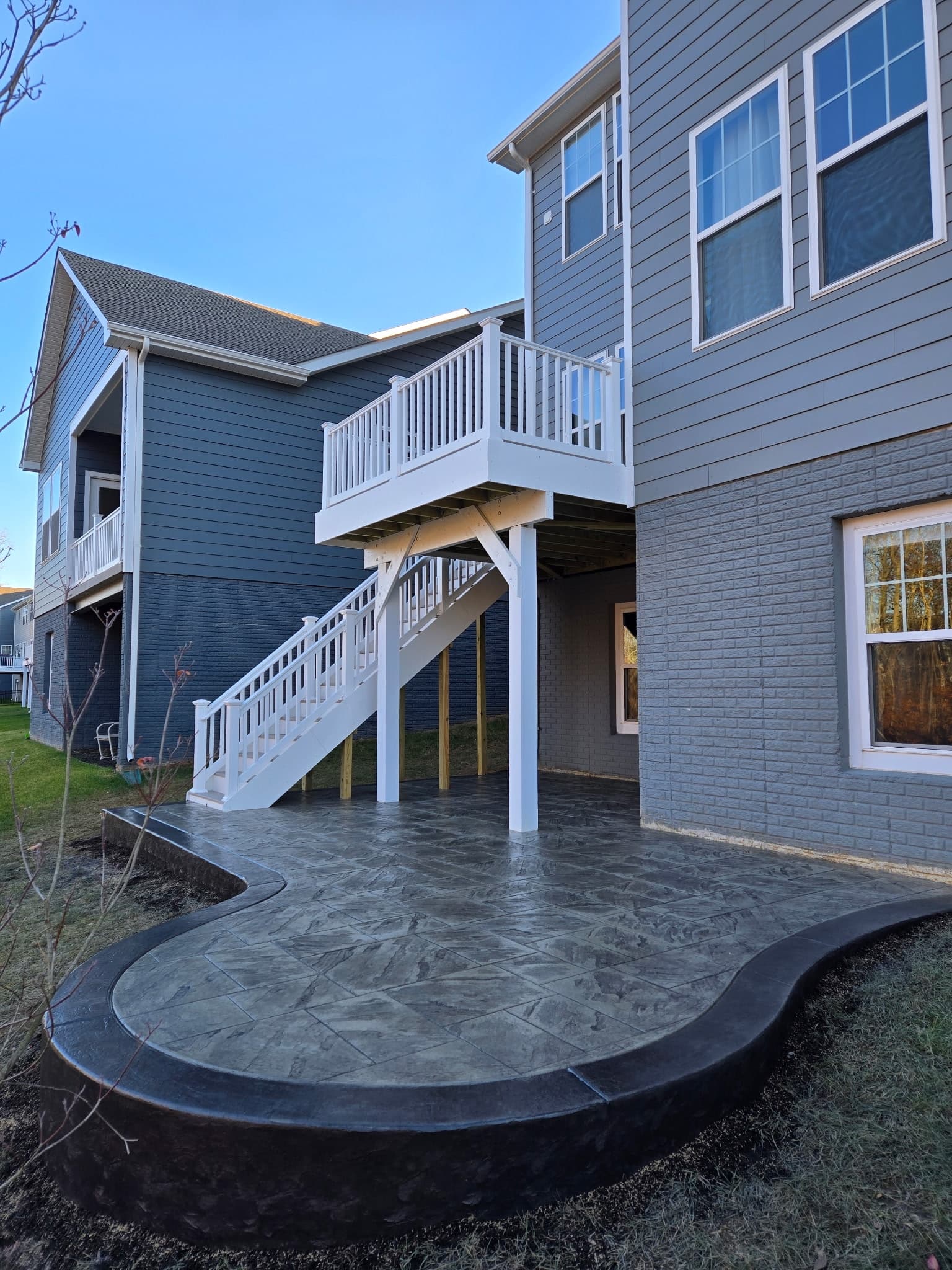 Curved stamped concrete patio beneath a two-story deck and stairs in South Riding