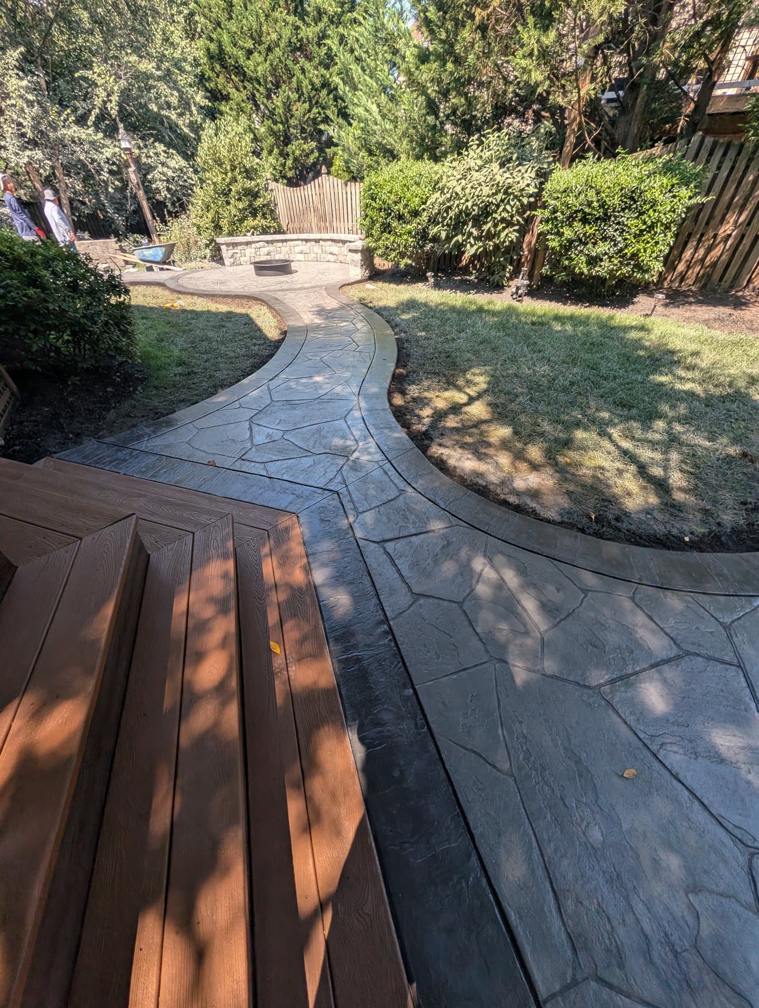 Stamped concrete walkway meeting a wood deck staircase, with the circular patio and fire pit visible in the background