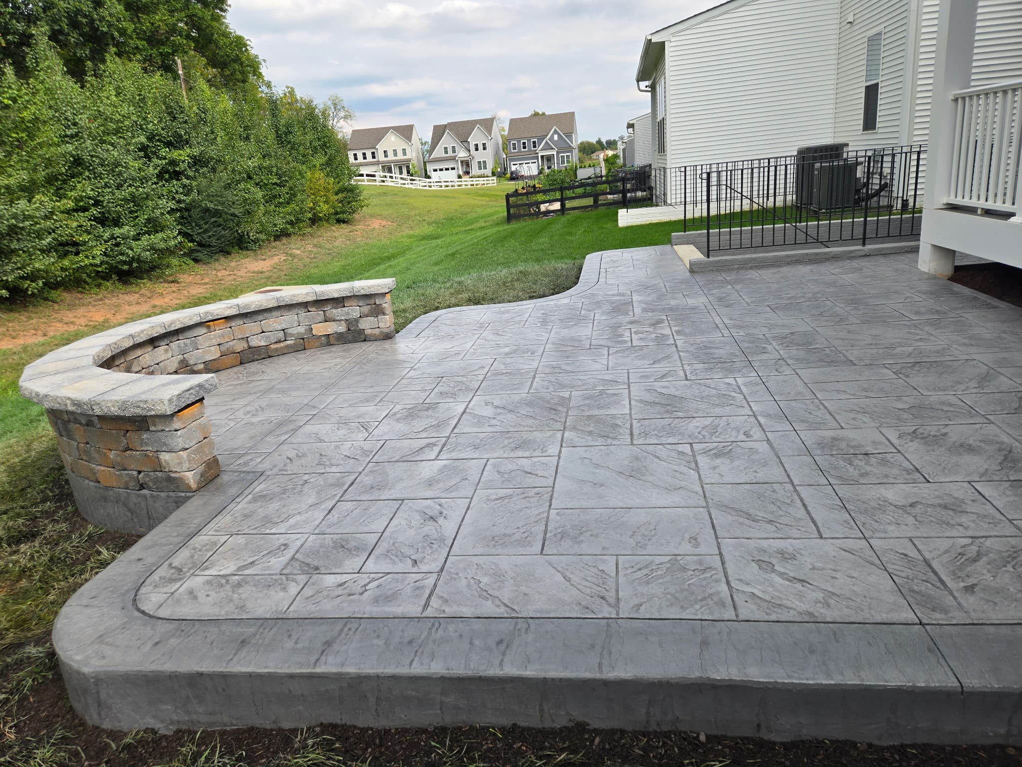 Finished gray flagstone-pattern stamped concrete patio in Aldie, VA, with a curved stone seating wall, wide view