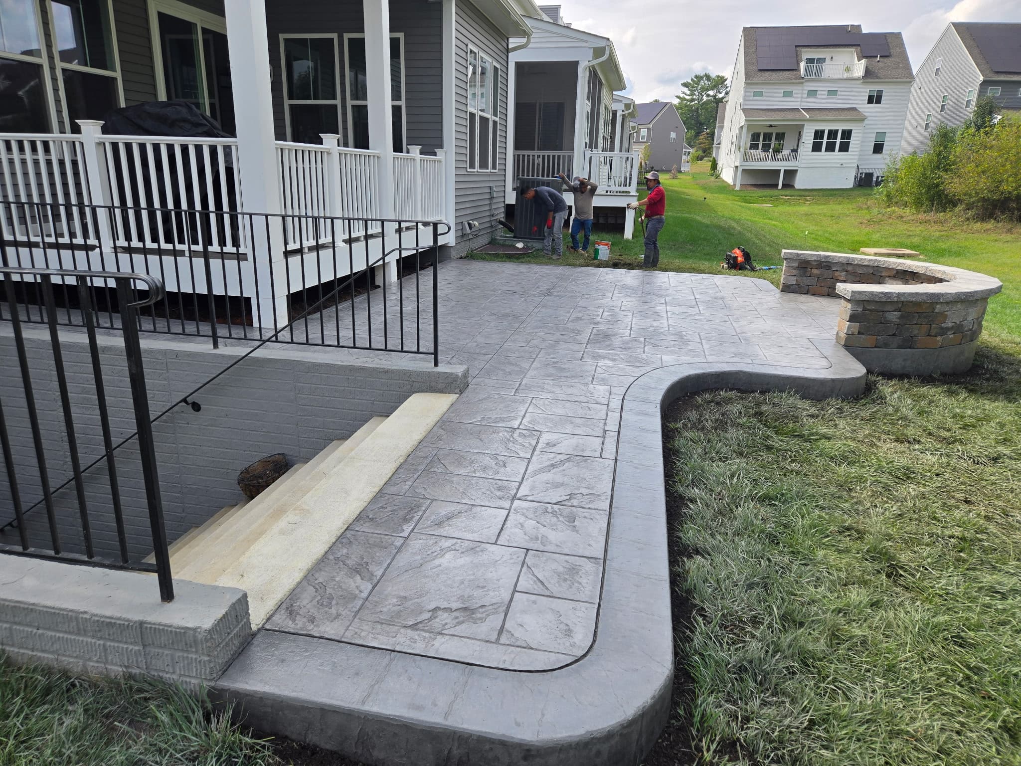 Workers finishing the edges of a freshly poured stamped concrete patio in Aldie, VA, next to a home's deck