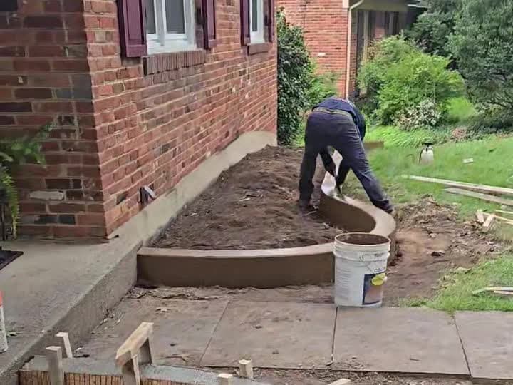 Worker hand-finishing curved colored concrete landscape curbing in Oakton, VA, next to a brick home