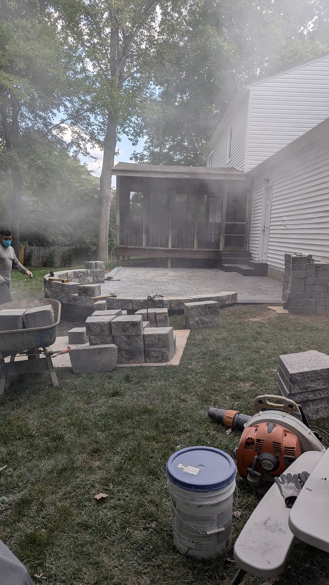Curved stone seating wall under construction around a freshly poured stamped concrete patio