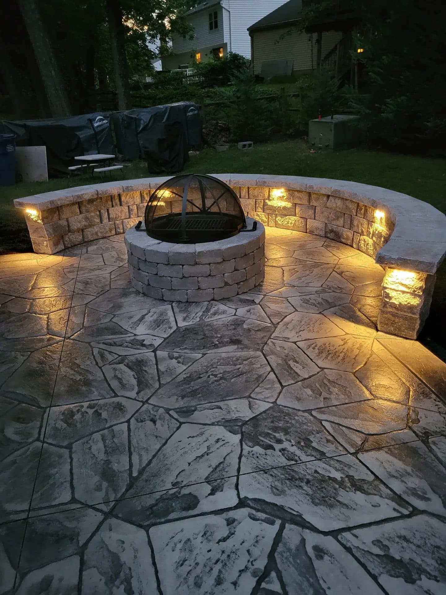 Finished stamped concrete patio with a curved stone seating wall and built-in lighting, evening
