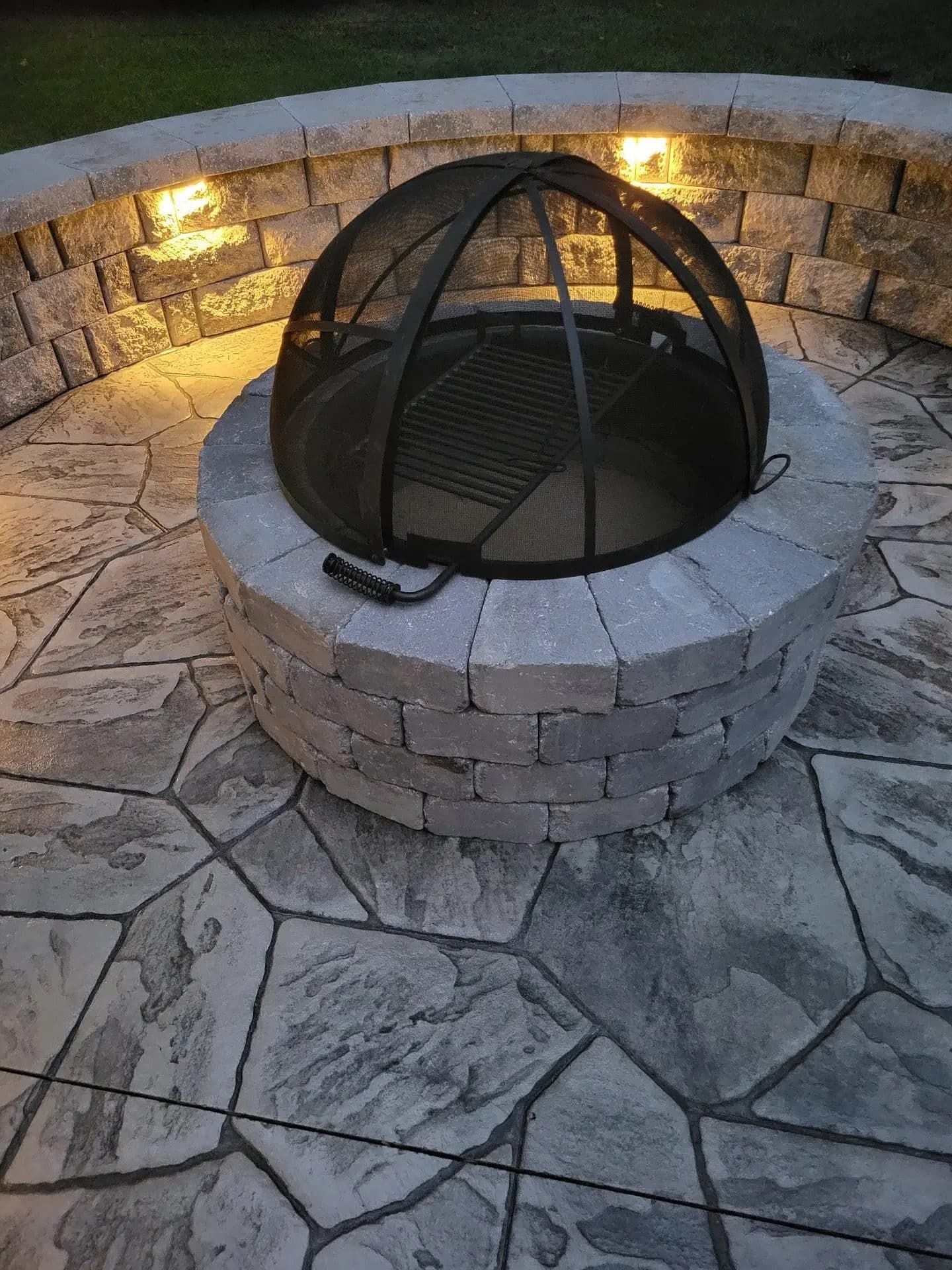 Fire pit with a spark screen cover on the finished stamped concrete patio, evening