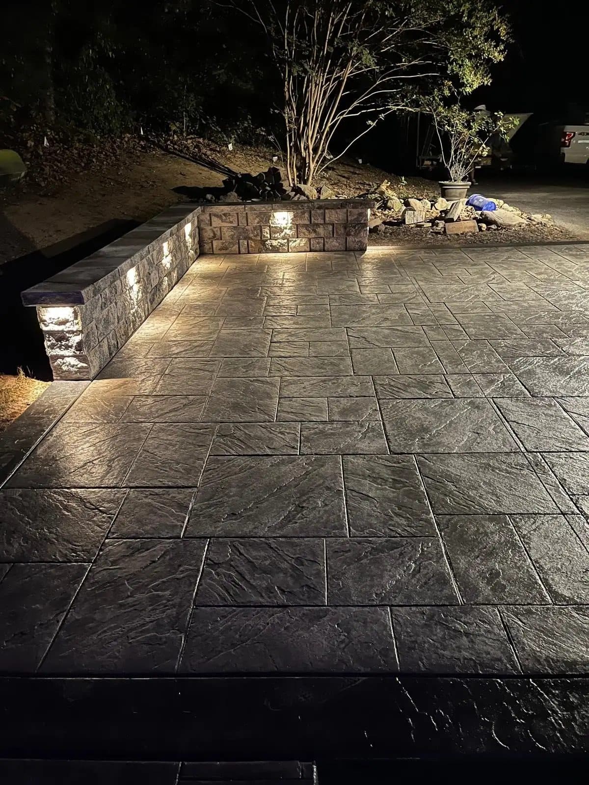 Retaining wall with built-in lighting alongside a dark ashlar-pattern stamped concrete patio, evening