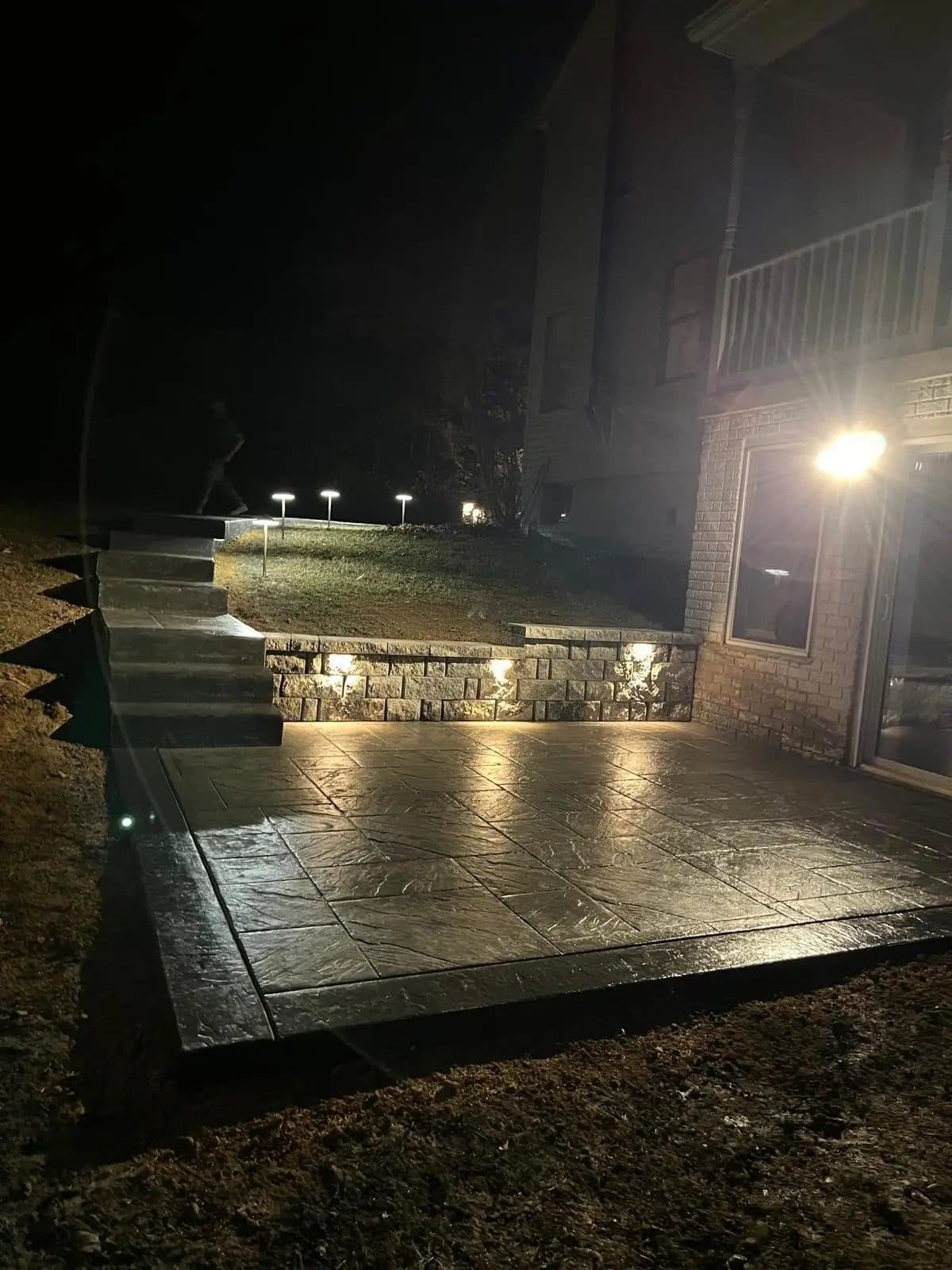 Stamped concrete patio steps and retaining wall with accent lighting, evening