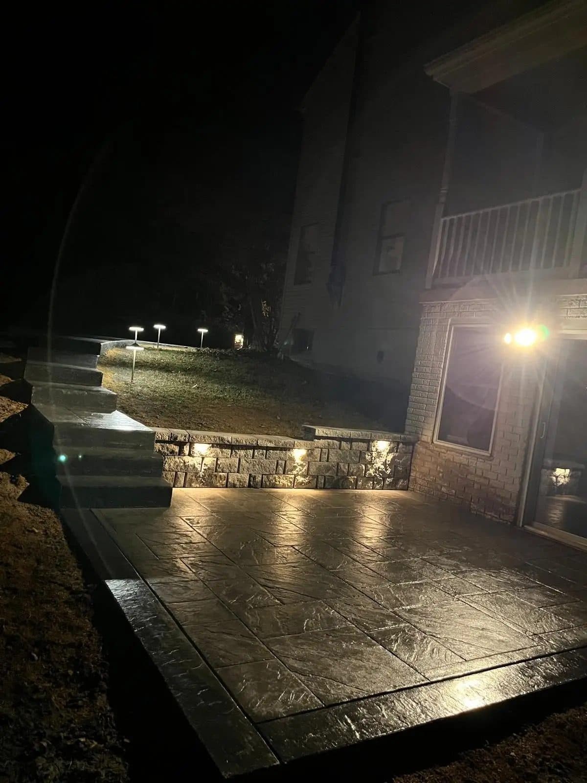 Retaining wall and stamped concrete patio alongside a home's walkout level, evening