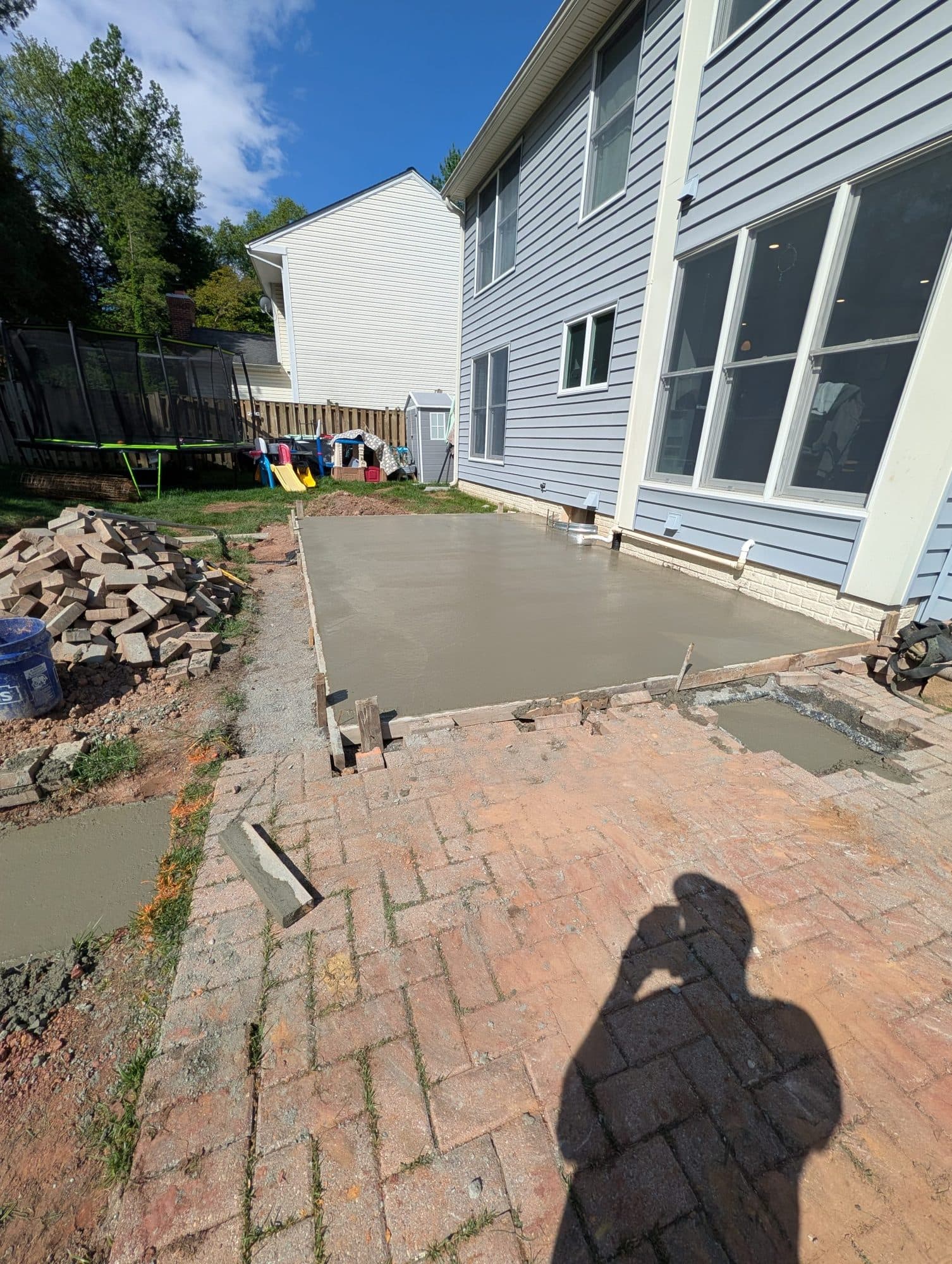 Brushed concrete patio slab poured alongside a screened-in porch addition, daytime