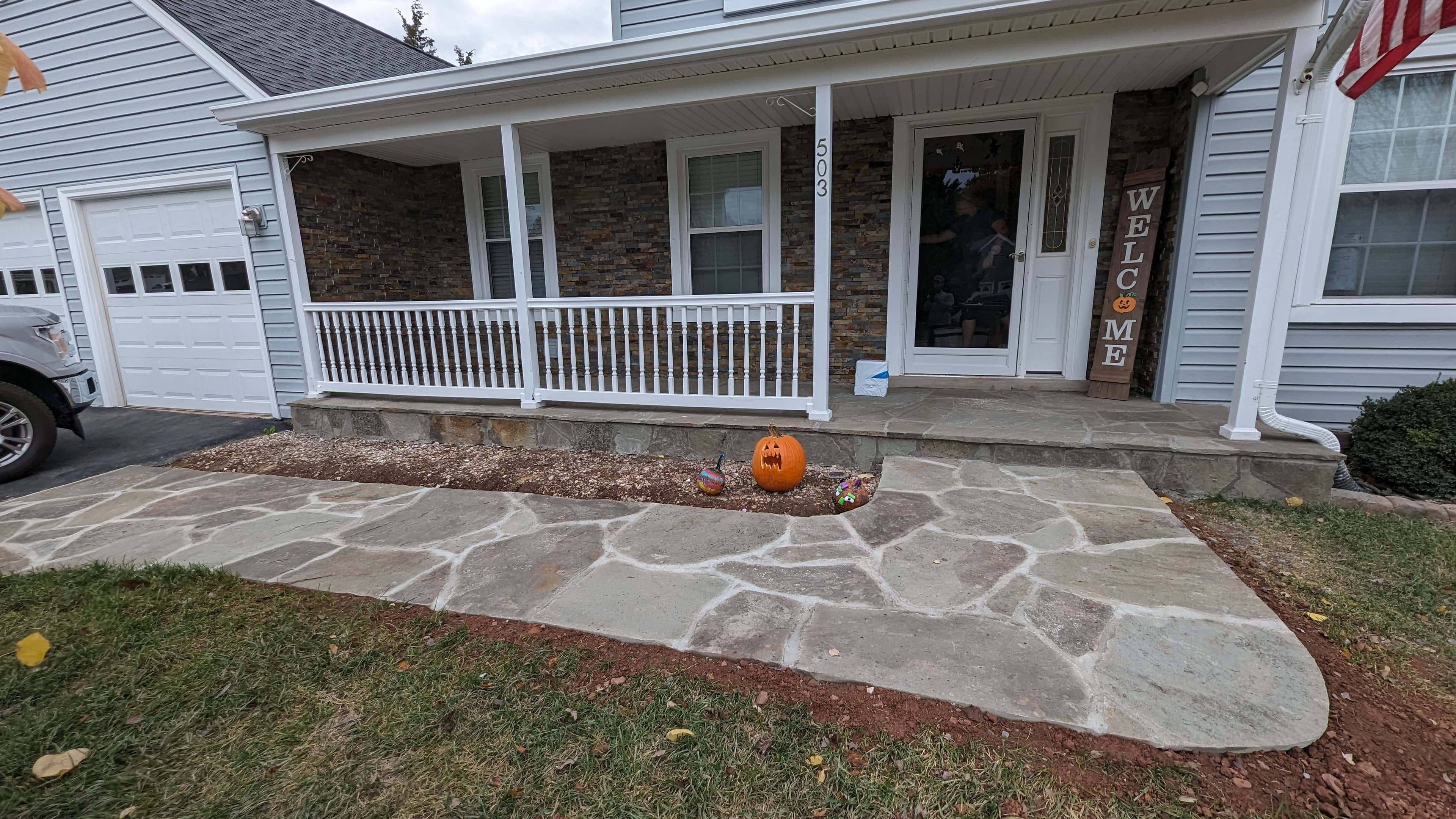 Finished front porch with stacked stone veneer facade, white railings, and a flagstone walkway leading to the entrance