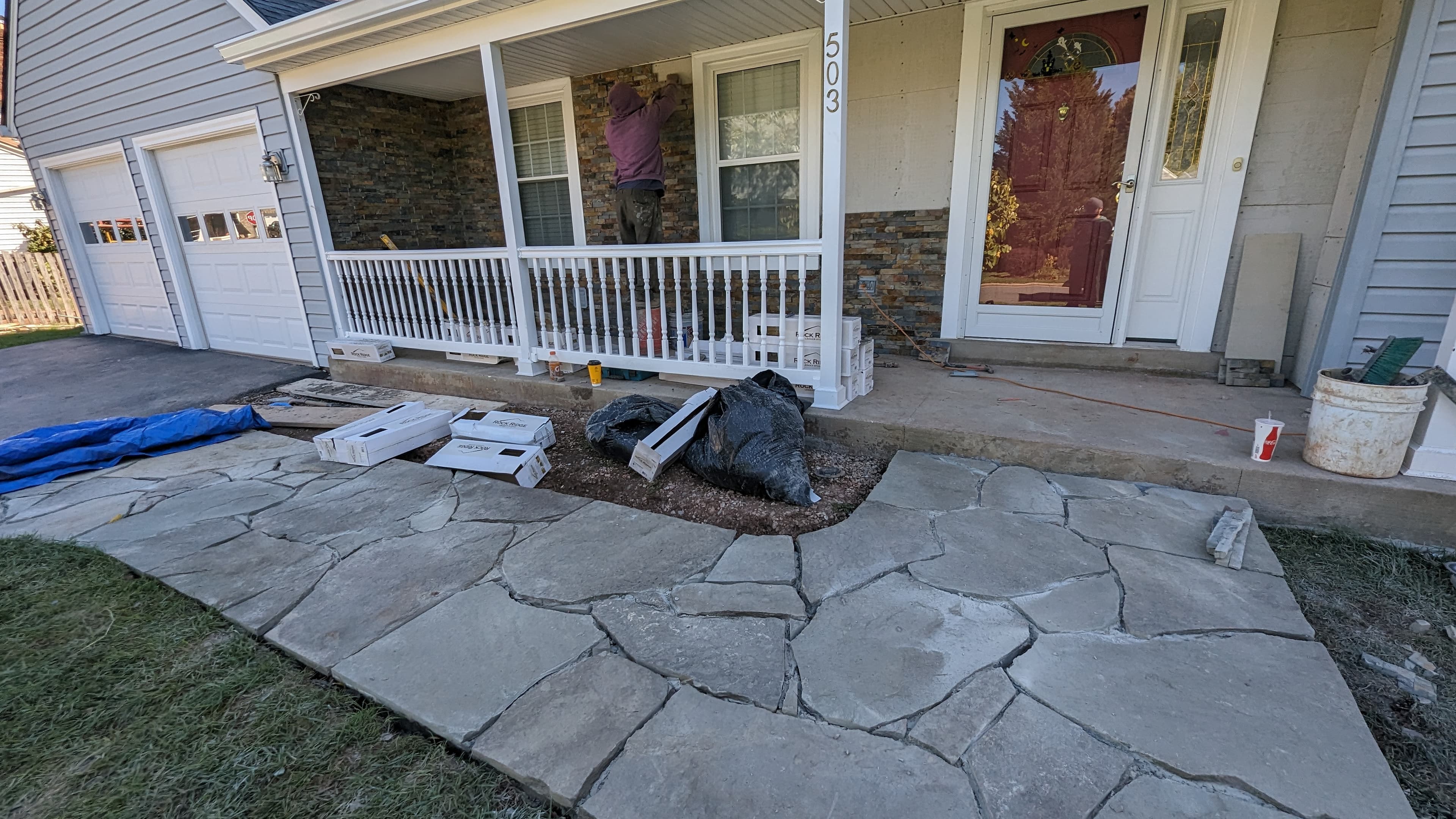 Flagstone walkway being laid alongside a stone veneer porch facade in progress