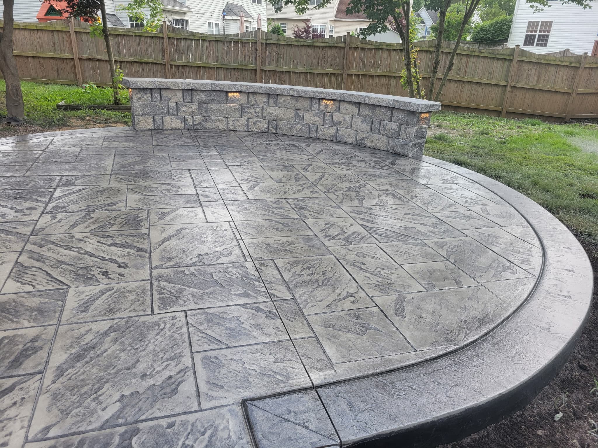 Curved stone seat wall with integrated lighting along a stamped concrete patio in South Riding