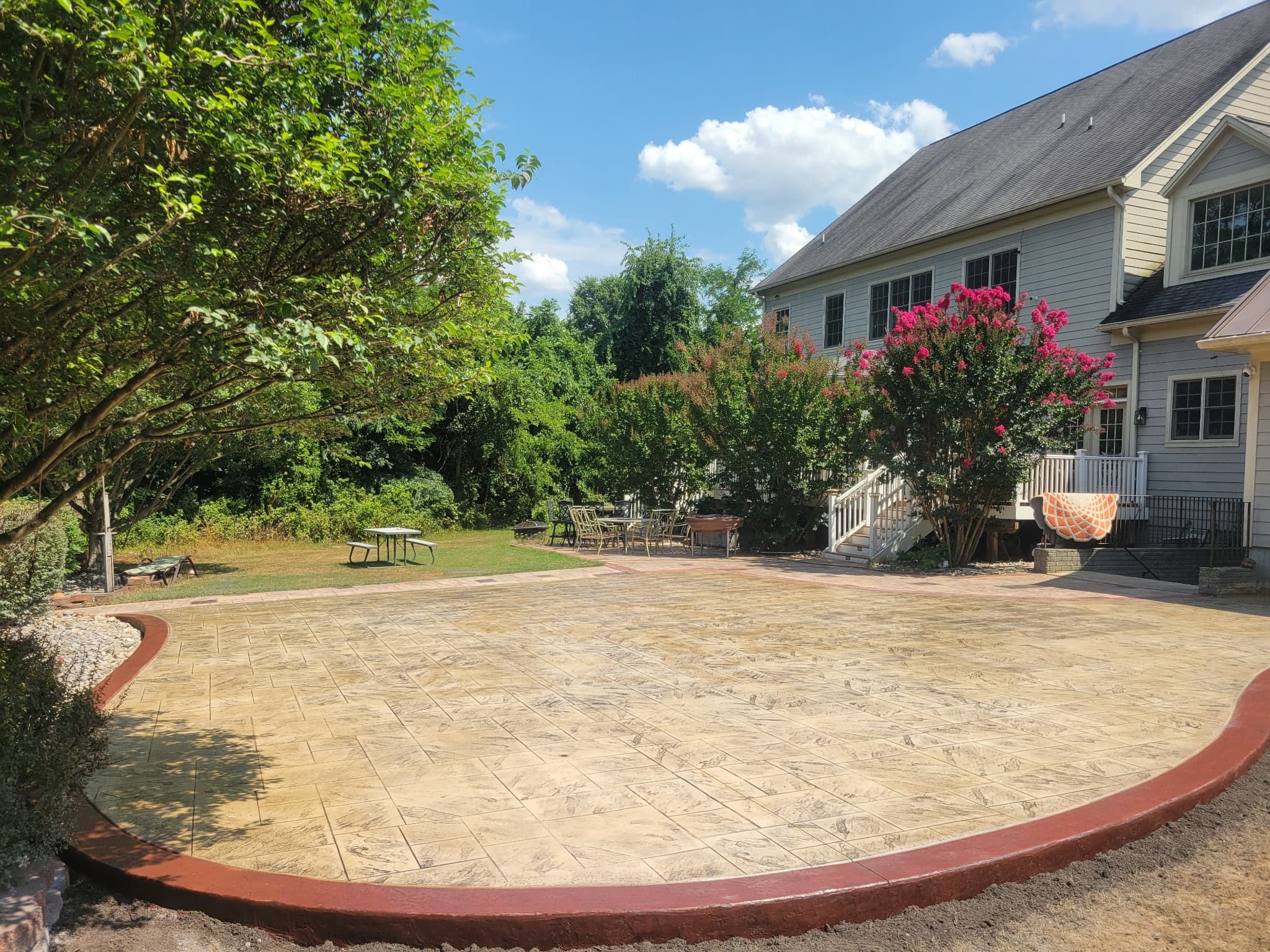 Large stamped concrete patio connecting to a paver walkway and deck stairs in Chantilly