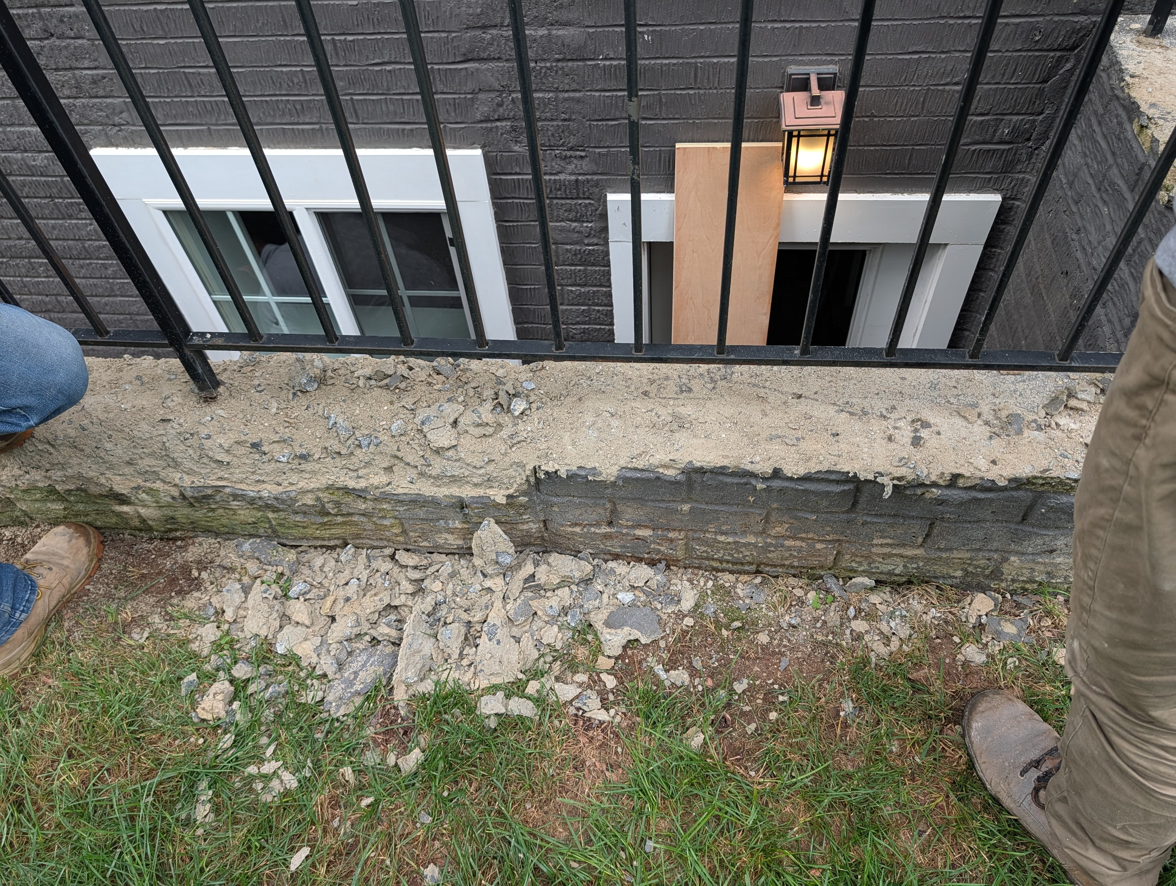 Deteriorated, spalling concrete wall cap next to a basement window well, with broken concrete debris on the ground below