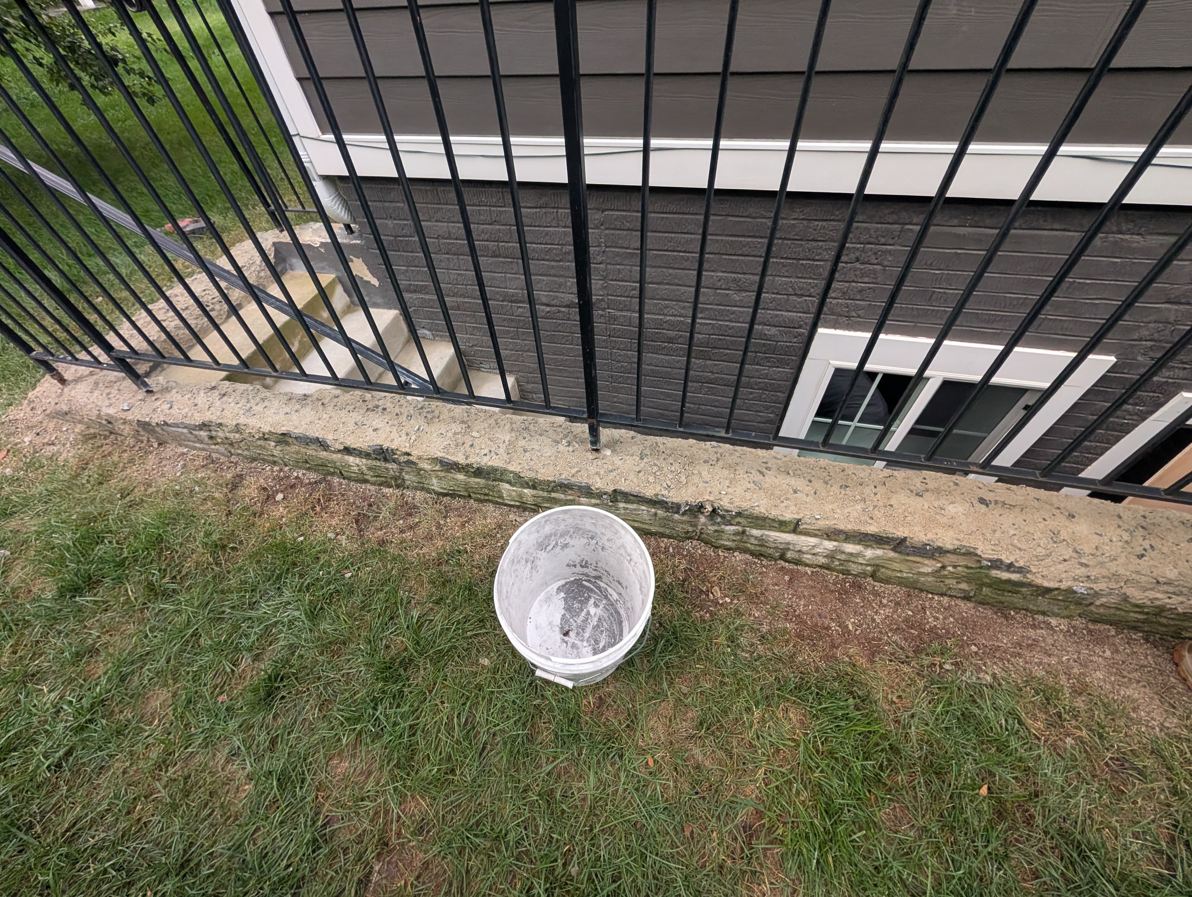Deteriorated concrete wall cap along a walkout basement stairwell, with a bucket set on top during prep