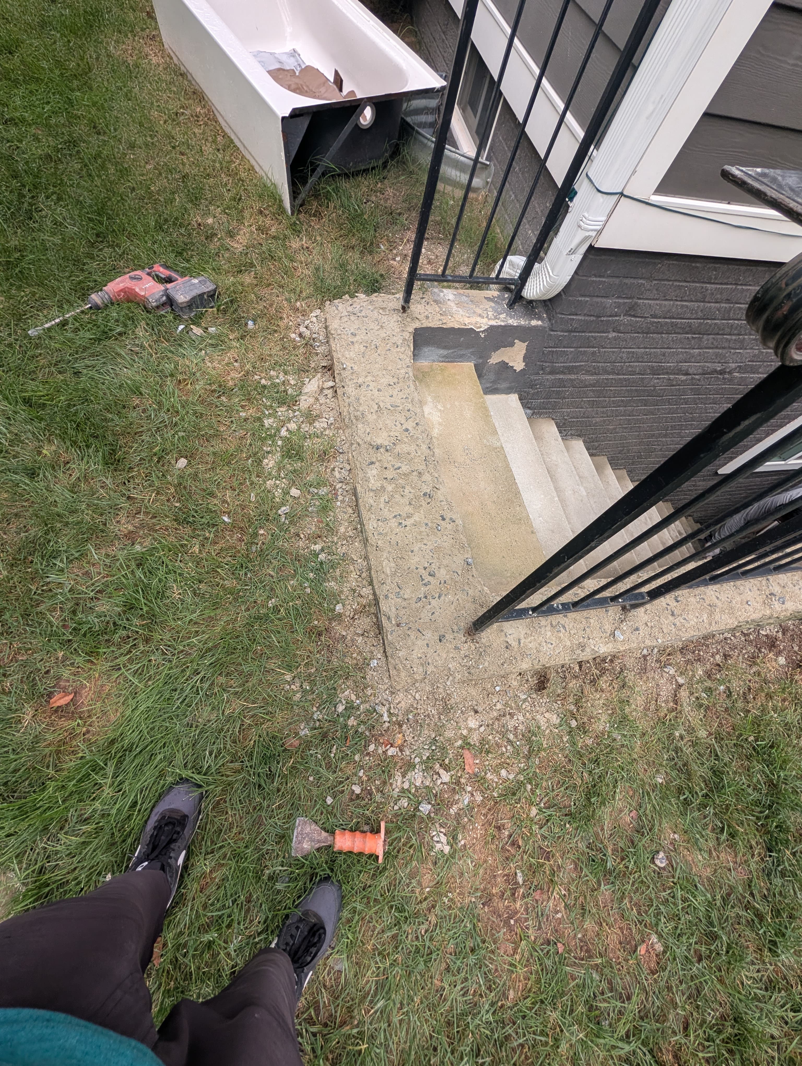 Walkout basement stairwell before repair, with a worn, patched stair surface and a removed bathtub set to the side