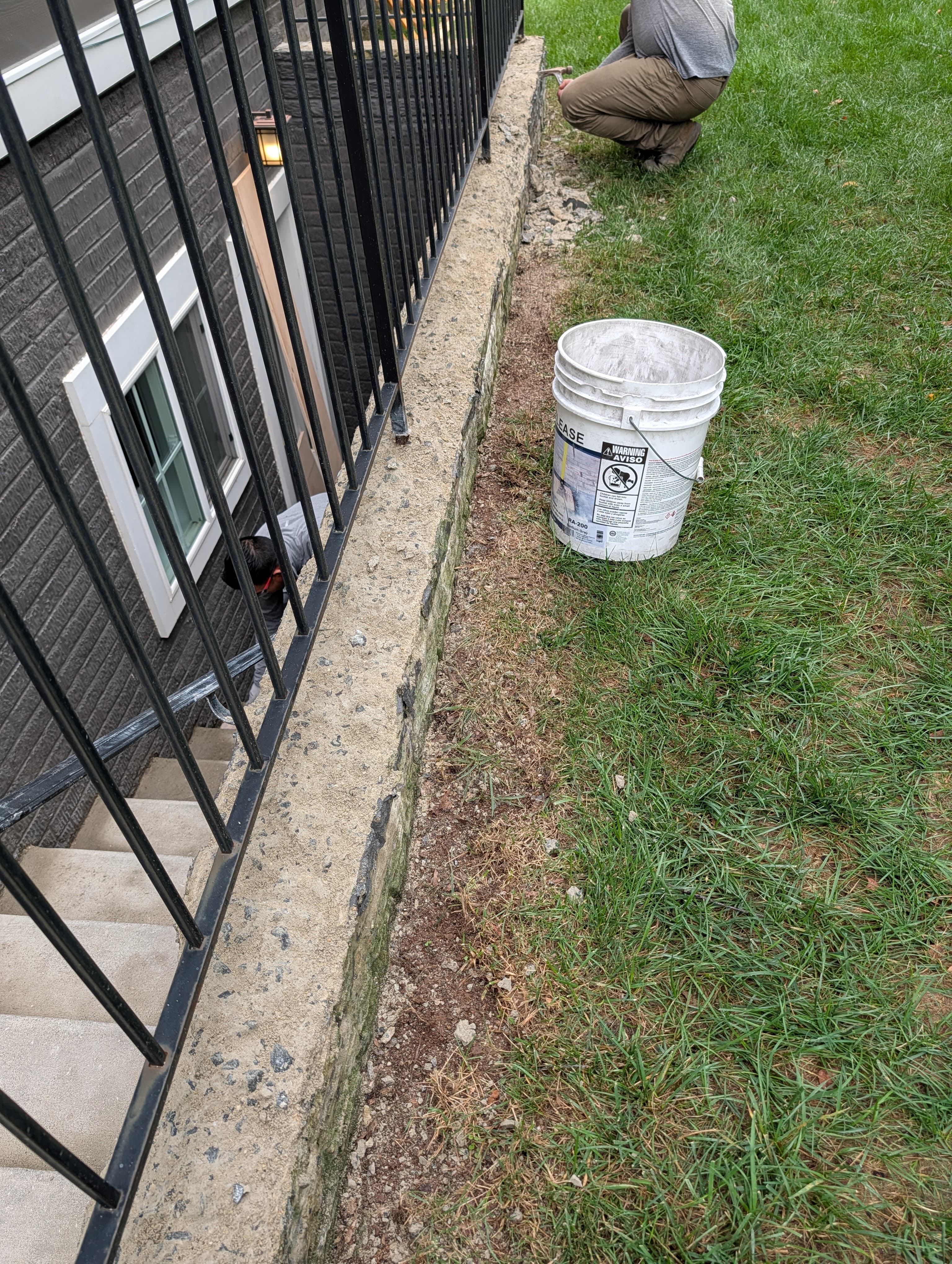 Worker applying concrete repair material to the deteriorated wall cap along the basement stairwell