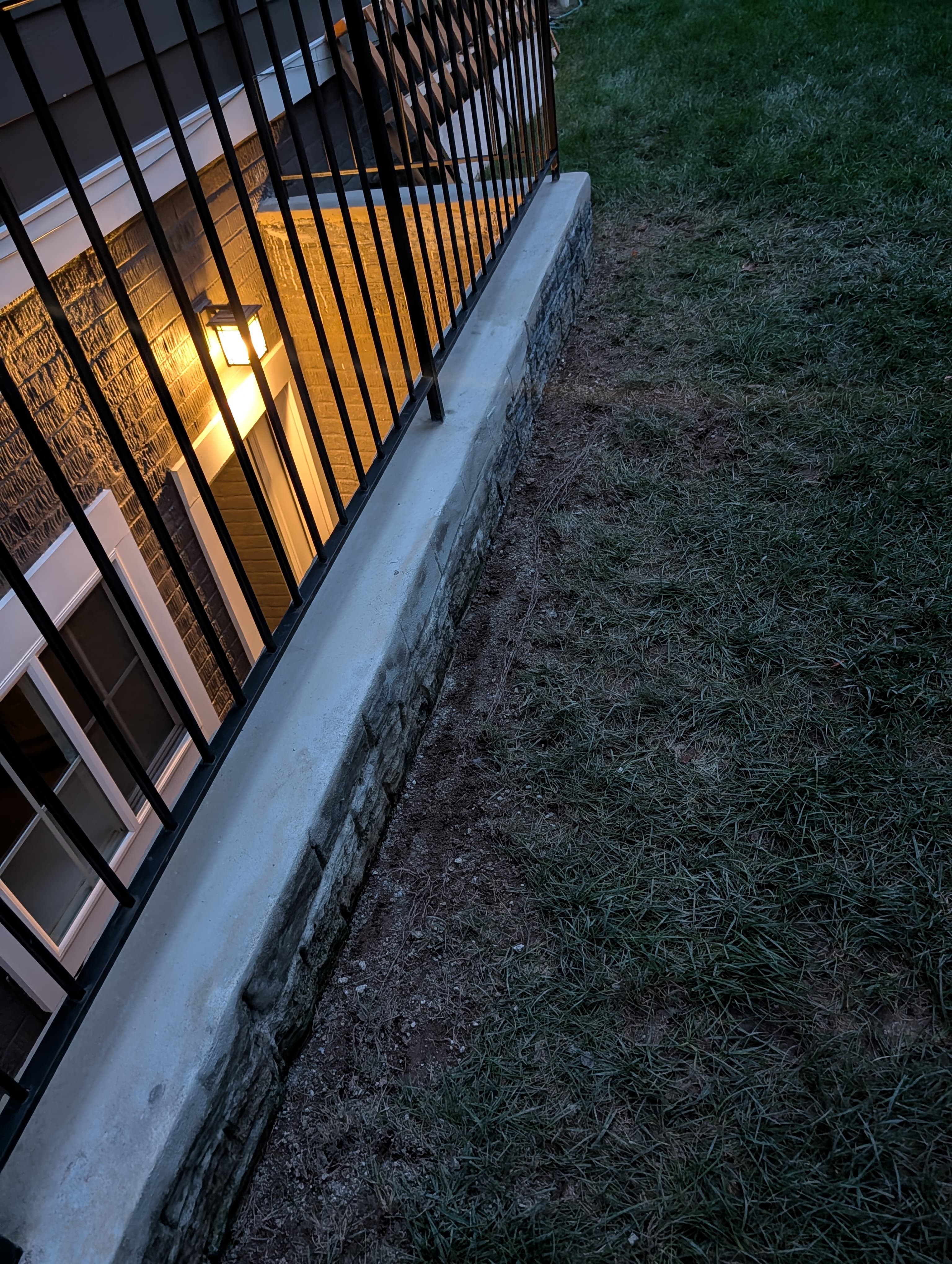 Resurfaced concrete wall cap corner along the basement stairwell, evening, lit by an exterior sconce
