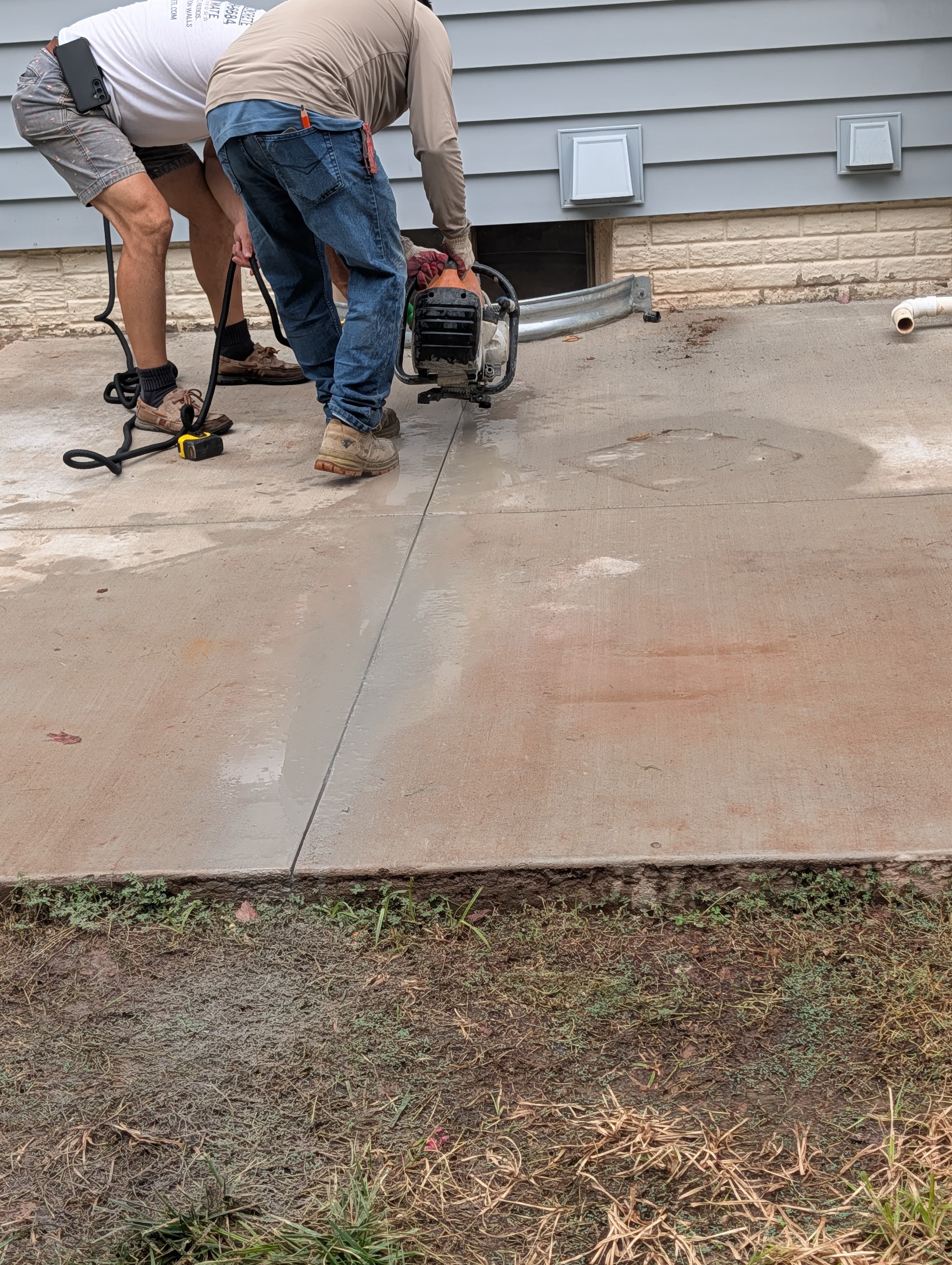 Two workers guiding a gas-powered concrete saw across an existing slab during a cut